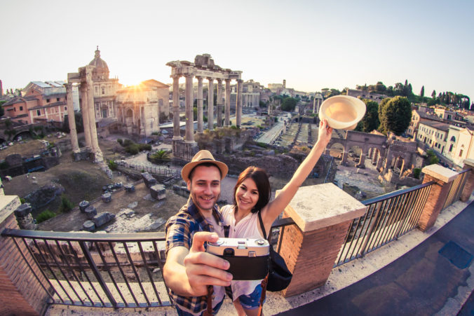 Young couple tourist looking at Roman Forum at sunrise and kissing taking selfie. Historical imperial Foro Romano in Rome, Italy from panoramic point of view.