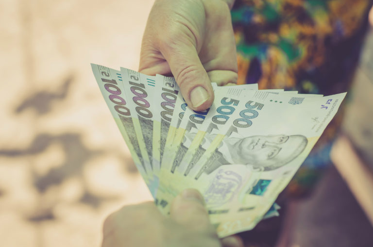 A man is concealing money to a pensioner. Help concept for poor people. A man gives an elderly woman Ukrainian hryvnia money.