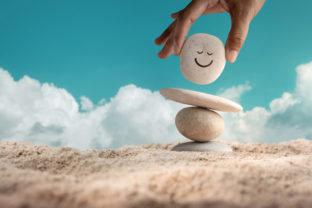 Enjoying Life Concept. Harmony and Positive Mind. Hand Setting Natural Pebble Stone with Smiling Face Cartoon to Balance on Beach Sand