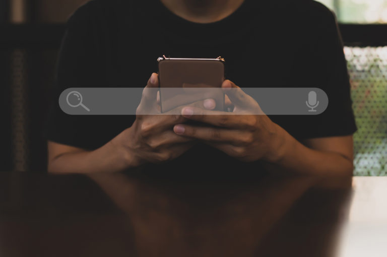 Young asian man wearing black t shirt sitting on desk hand holding smartphone to Searching for information. Using Search Console with your website.