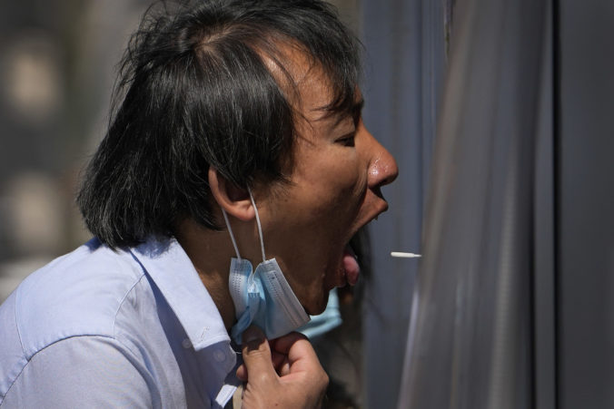 Virus Outbreak China A worker pulls his mask to get a throat swab sample taken at a coronavirus testing site, Sunday, April 3, 2022, in Beijing. COVID 19 cases in China's largest city of Shanghai are still rising as millions remain isolated at home under a sweeping lockdown