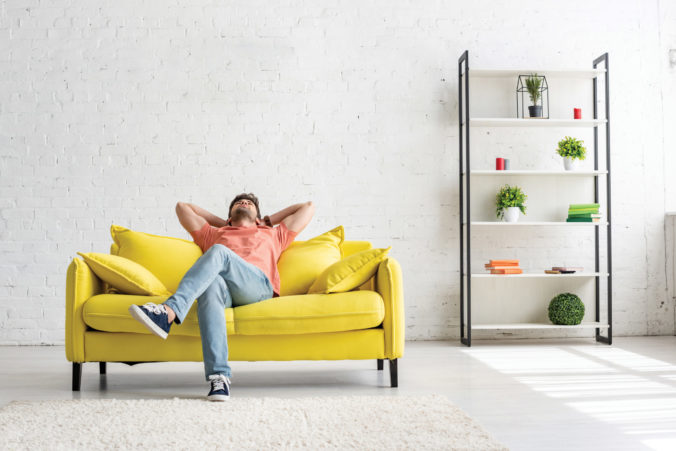 Young,Man,Sitting,On,Yellow,Sofa,Under,Air,Conditioner,In