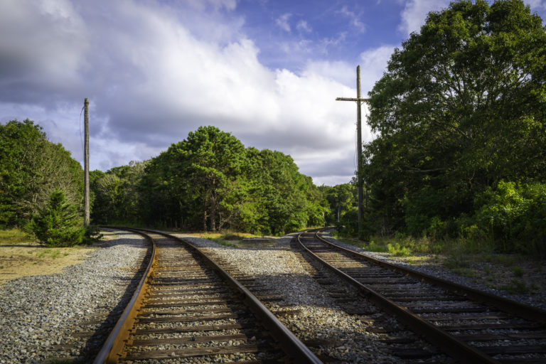 Rustic railway tracks are divided into two. Dramatic cloudscape over the old train tracks with a cross like post over the forest on Cape Cod.