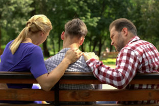 Caring mother and dad supporting sad teen son sitting on bench i