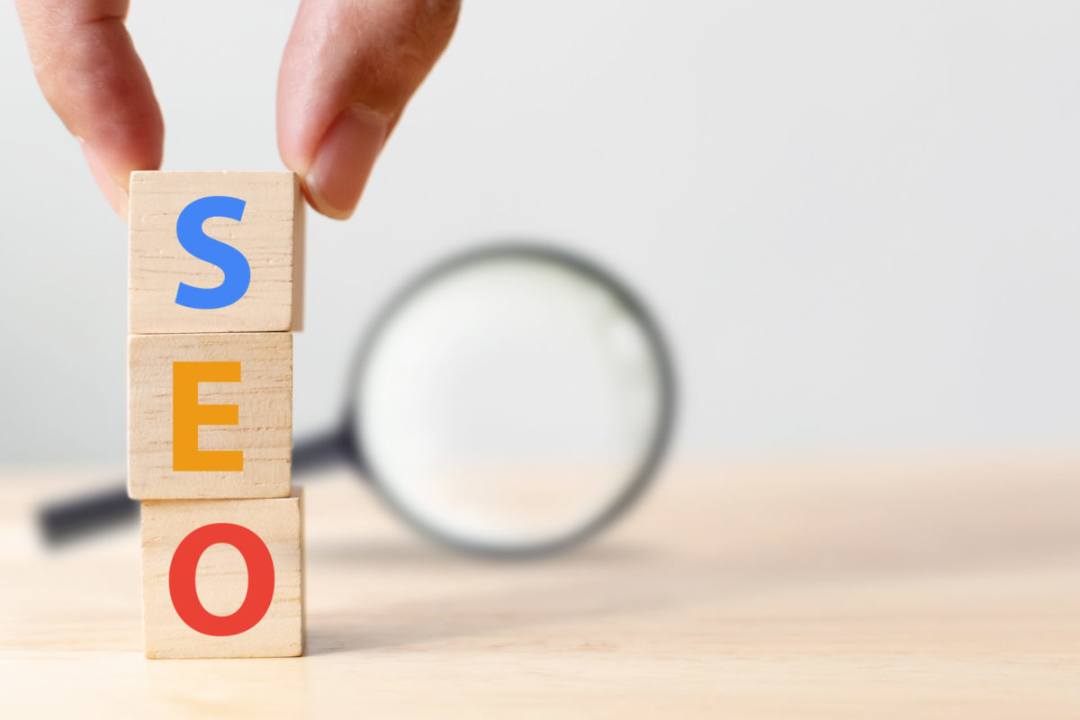 SEO, Search engine optimization concept. Hand putting wood block cube shape with word SEO and magnifying glass