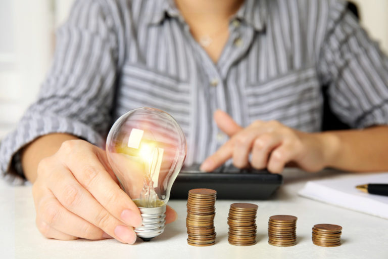 Woman with light bulb, calculator and coins at white table, clos