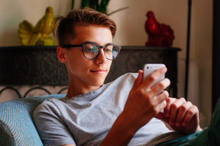 Smiling boy in glasses using smartphone