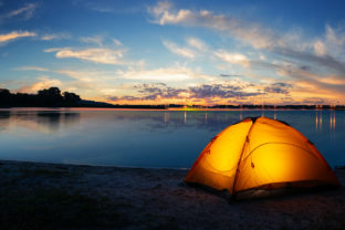 Orange tourist lit tent by the lake at sunset