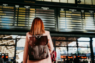 Young woman at train station looking at destination board. Travel and public transport concept