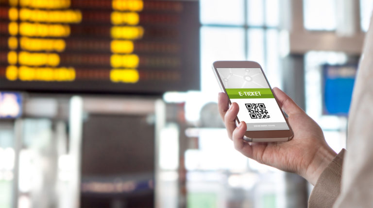 Buying online ticket from internet. E ticket on mobile phone screen with schedule in the blurred background. Universal public transportation terminal. Bus, train, metro, subway or underground station