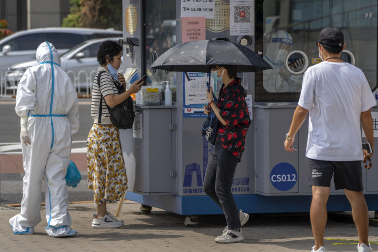 A worker wearing a protective suit sprays disinfectant as a woman waits to have her throat swabbed for a COVID-19 test at a coronavirus testing facility in Beijing