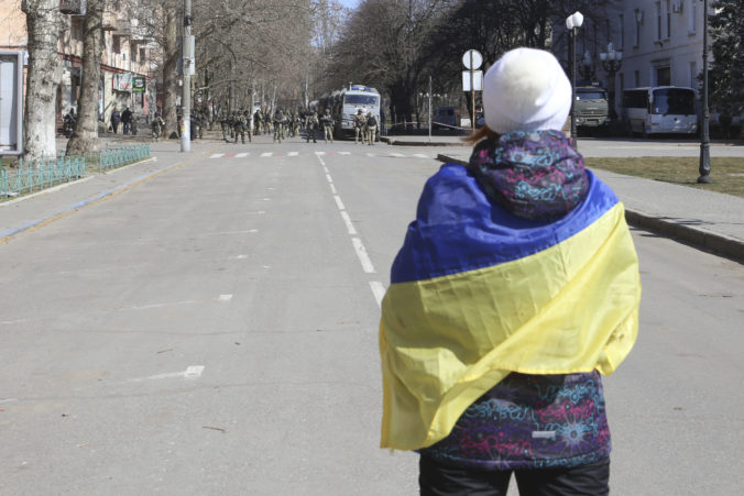 FILE - A woman covered by Ukrainian flag stands in front of Russian troops in a street during a rally against Russian occupation in Kherson, Ukraine, on March 19, 2022. According to Russian state TV, the future of the Ukrainian regions occupied by Moscow's forces is all but decided: Referendums on becoming part of Russia will soon take place there, and the joyful residents who were abandoned by Kyiv will be able to prosper in peace. In reality, the Kremlin appears to be in no rush to seal the deal on Ukraine's southern regions of Kherson and Zaporizhzhia and the eastern provinces of Donetsk and Luhansk