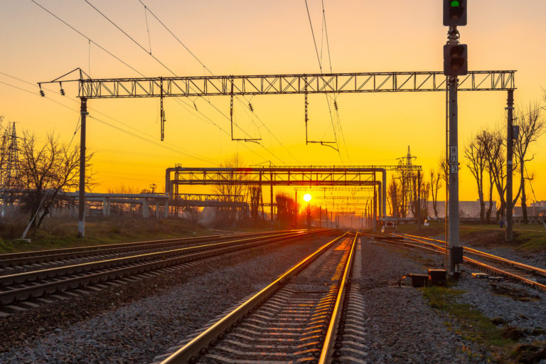 Railway station against beautiful sky at sunset. Industrial landscape with railroad, colorful blue sky with red clouds, sun, trees and green grass. Railway junction. Heavy industry. Evening in autumn