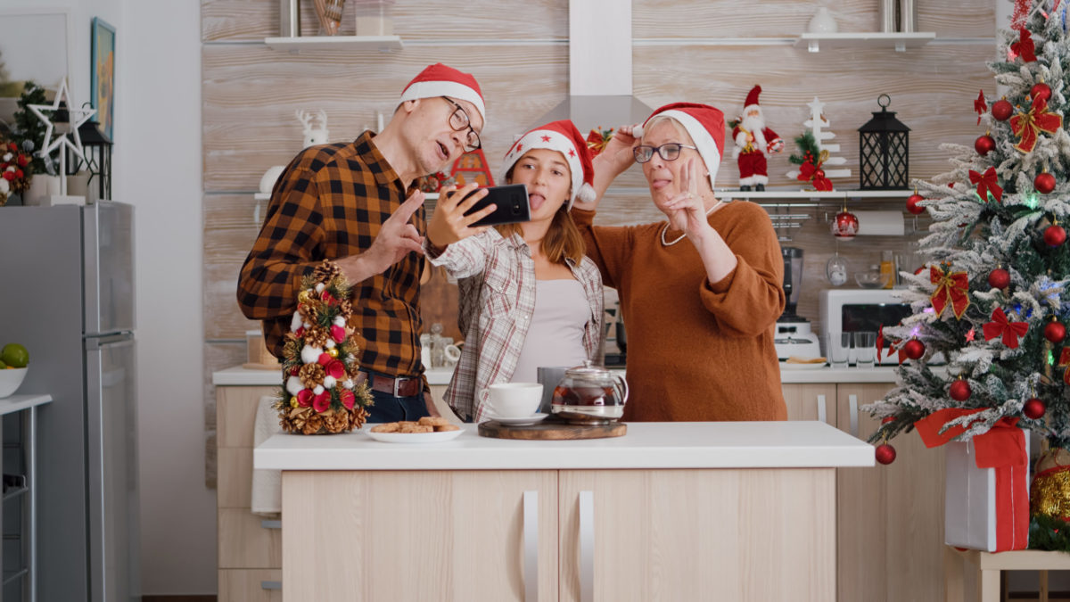 Family taking selfie using smartphone enjoying winter holiday in xmas decorated kitchen