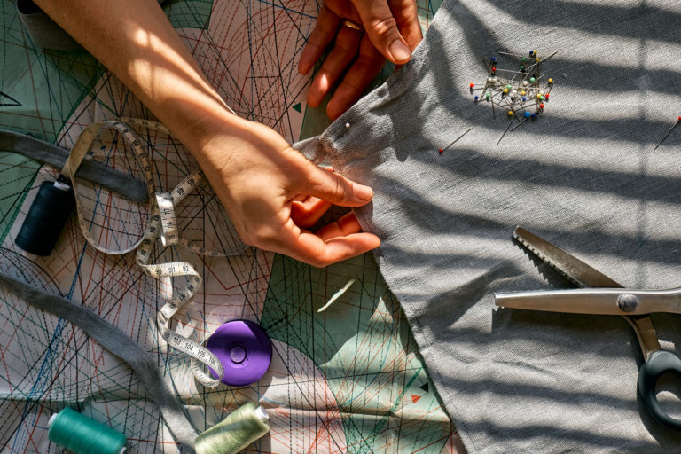 Woman is sketching pattern on a linen fabric Seamstress basting and sewing in a small studio Sartorial clothes Fashion studio, tailoring, handmade clothing concept Slow fashion Conscious consumption