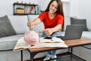 Young brunette woman putting euro coin in piggy bank saving for travel smiling happy pointing with hand and finger