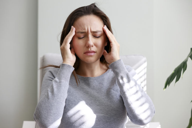 Shot of a young woman holding her head in discomfort due to pain at home
