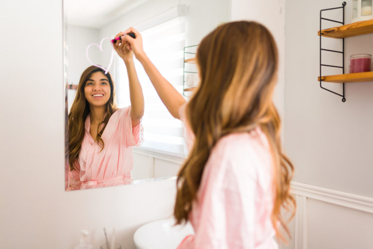 Lovely woman with a good self esteem using a lipstick to draw a heart in the mirror