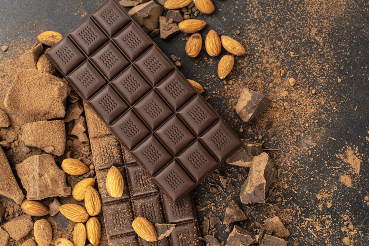 Cooking chocolate bars with almonds, handmade sweets. Composition of bars and pieces of dark almond chocolates on black background, top view. Pastry craft on the table chocolate background