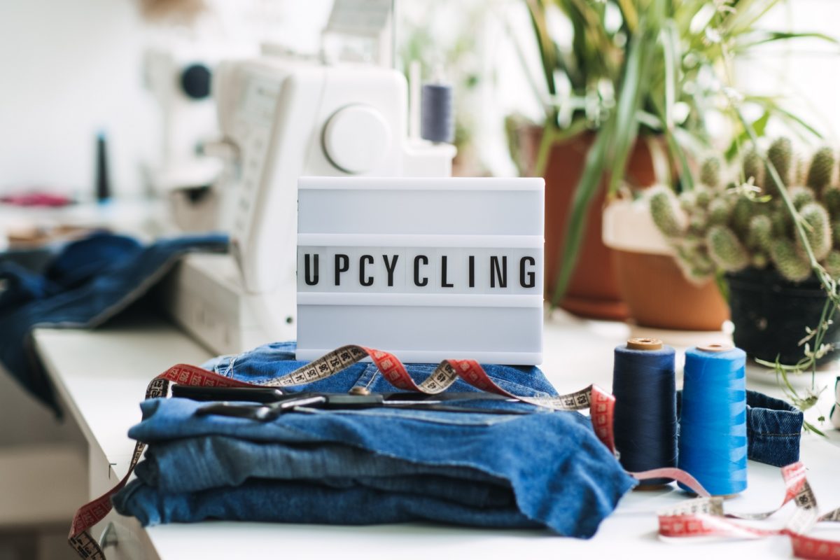 Denim Upcycling Ideas, Using Old Jeans, Repurposing Jeans, Reusing Old Jeans, Upcycle Stuff. Lightbox with text Upcycling, Stack of old blue jeans, scissors, thread and sewing tools in sewing studio.