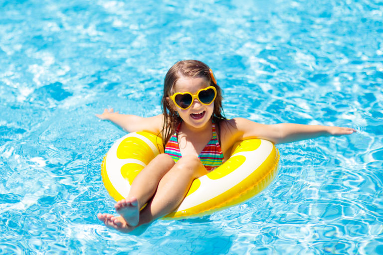 Child in swimming pool on ring toy. Kids swim.