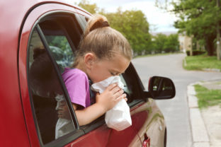 Little girl with paper bag suffering from nausea in car