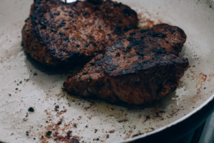 Overcooked beef steak lie on white frying pan