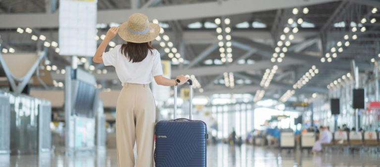 Young woman hand holding luggage handle before checking flight time in airport, Transport, insurance, travel and vacation concepts