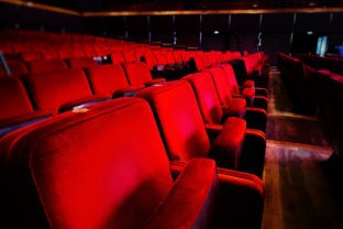 A row of empty red velvet armchairs inside an auditorium.