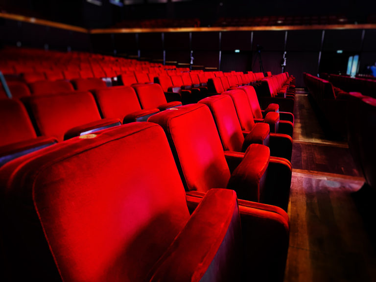 A row of empty red velvet armchairs inside an auditorium.