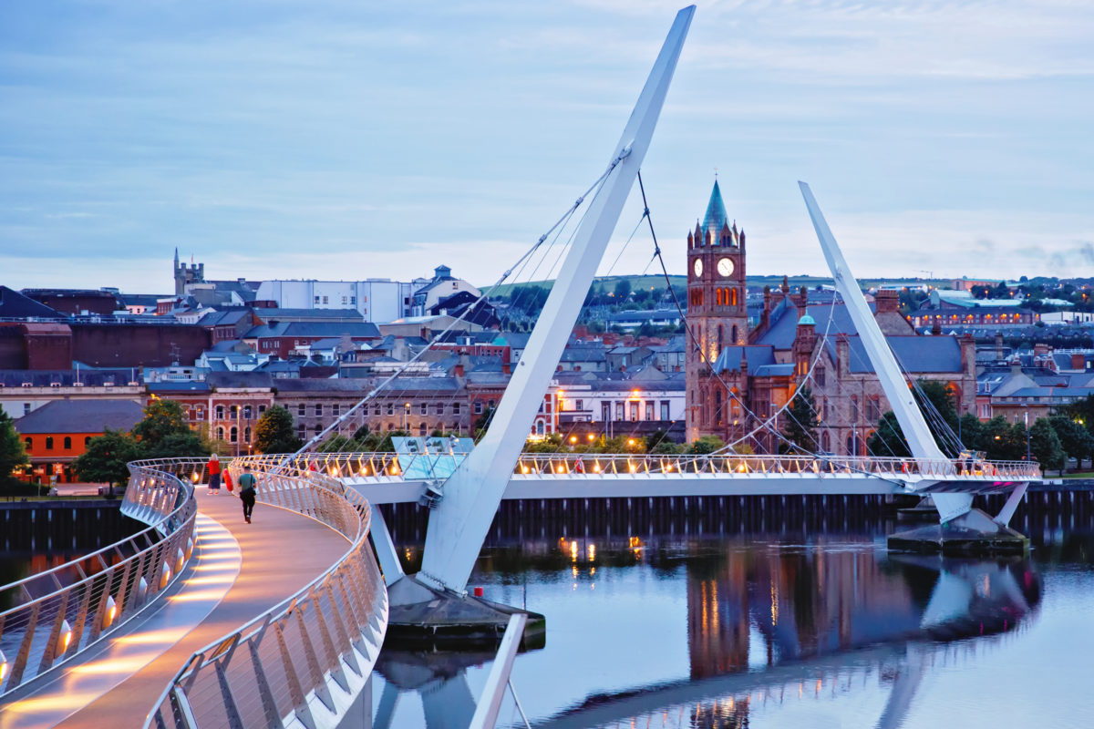 Derry, Ireland. Illuminated Peace bridge in Derry Londonderry, City of Culture, in Northern Ireland with city center at the background. Night cloudy sky with reflection in the river at the dusk