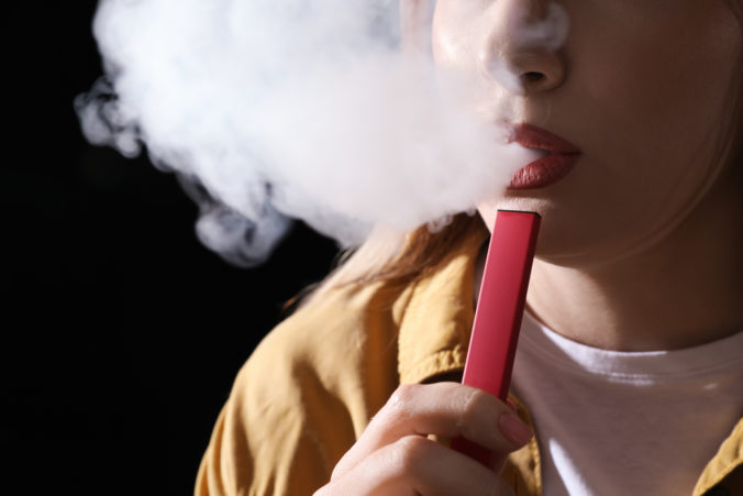 Young woman using electronic cigarette on black background, closeup