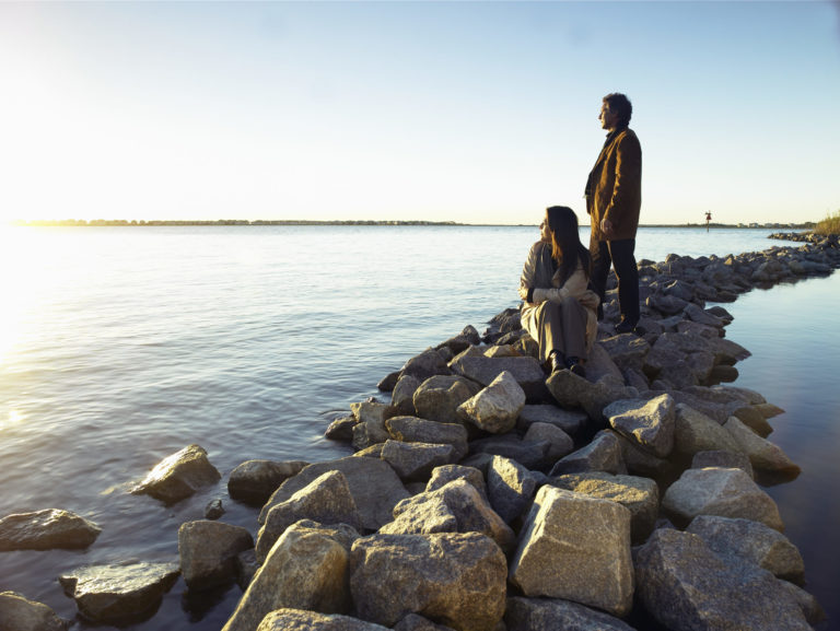 Mature couple watching sunrise on rock breakwater