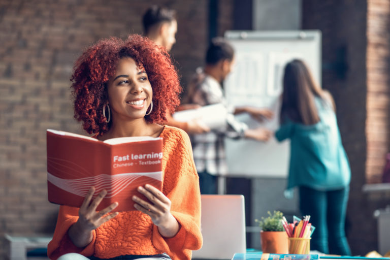 Cheerful student wearing orange sweater reading Chinese book