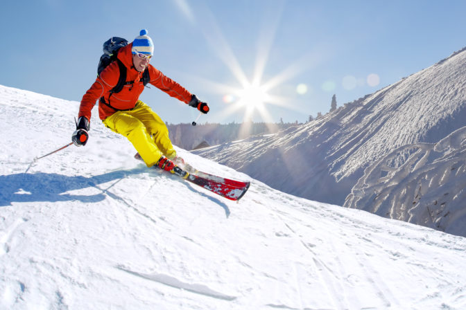 Skier skiing downhill in high mountains against blue sky.
