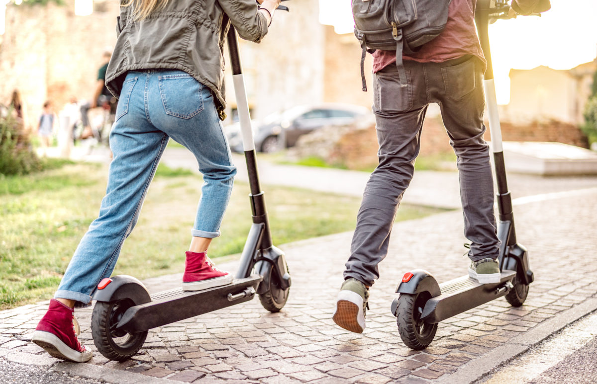 Millenial couple riding electric scooters at urban city park - Genz students using new ecological mean of transportation - Green eco energy concept with zero emission - Warm filter with sunshine halo