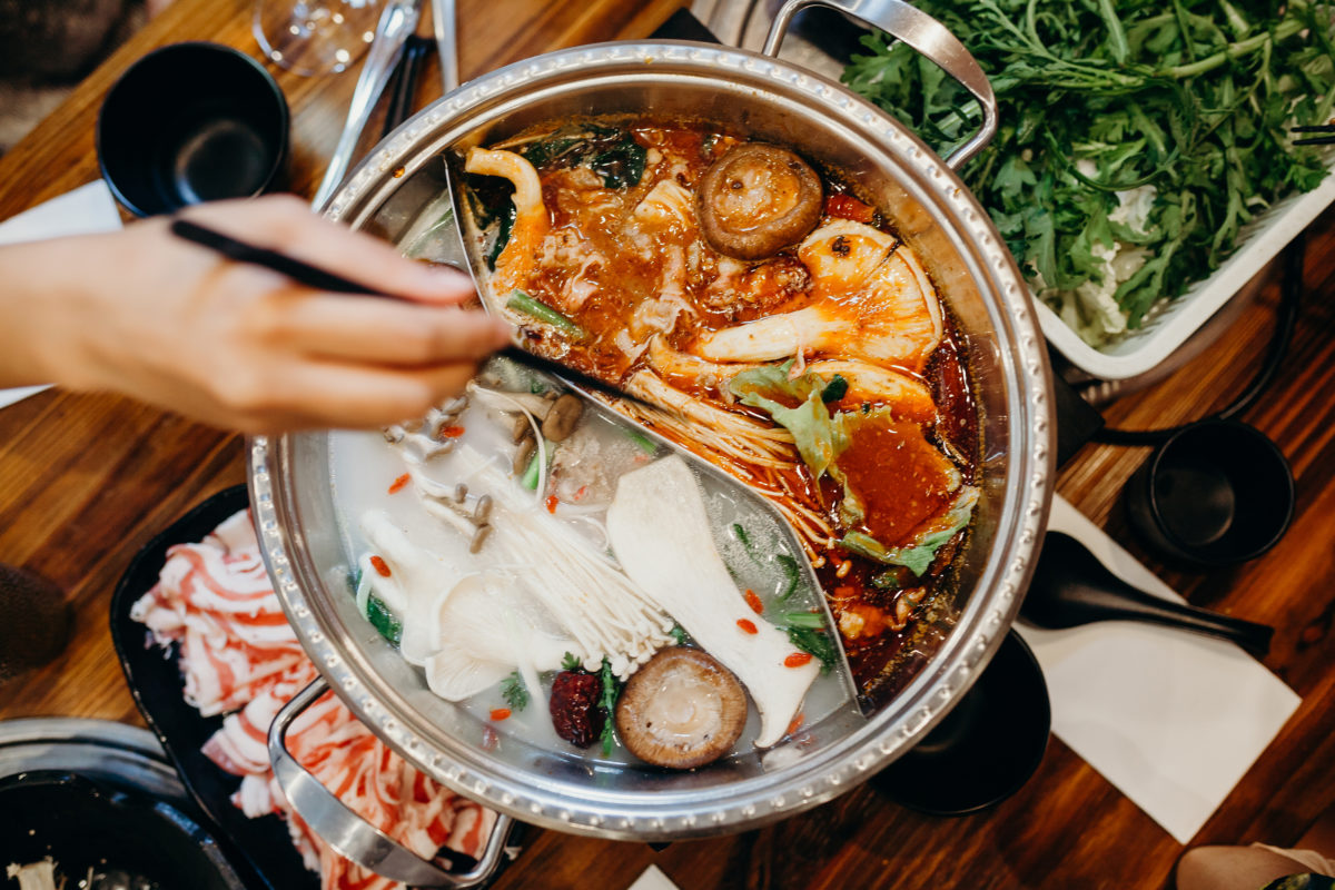 Korean hot pot meal. Hands taking food with chopsticks.
