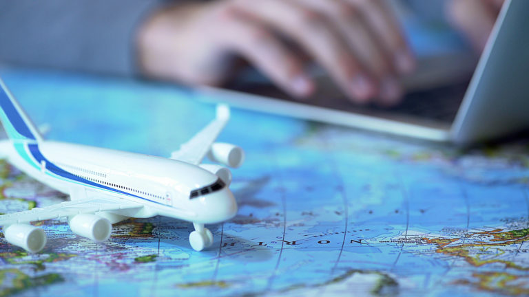 Airplane model closeup, defocused person booking flight tickets online on laptop
