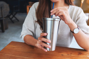 Closeup image of a woman drinking coffee in stainless steel cup
