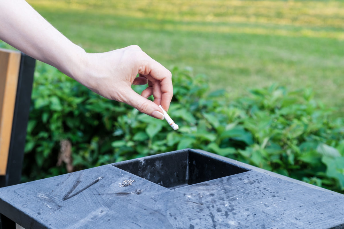 Woman throws her cigarette butt into a metal trash can in a city park