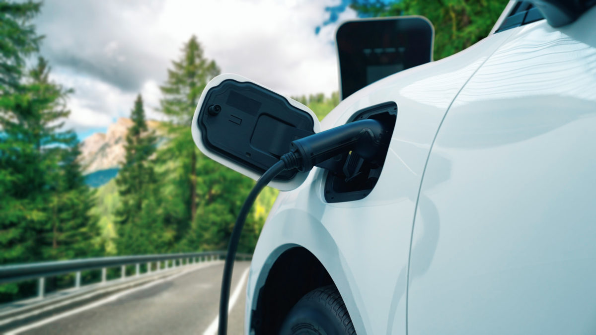 Progressive electric car in the green forest with charging station concept.