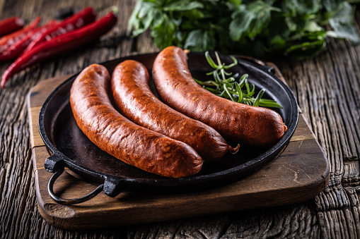 Pepper pork smoked sausages with rosemary in a cast iron pan.