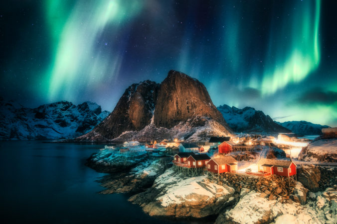 Aurora borealis, Northern lights over mountain with fishing village on coastline at Hamnoy, Lofoten islands
