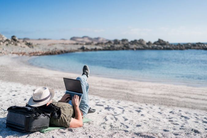Digital nomad lying on the beach outdoors alone working relaxed