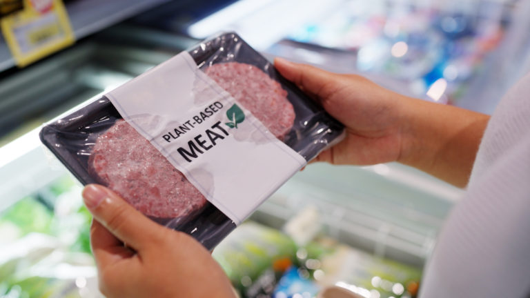 Close up hand carry choose zero pork soy bean faux peas cutlet gluten free read beyond non meat lab label. Buy raw fake beef tray in asia store veggie burger patty for health care eat diet meal cook.