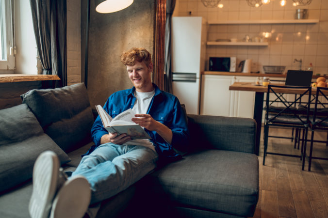 Ginger young man sitting at home at the window with a book