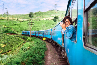 Happy smiling woman looks out from window traveling by train on most picturesque train road in Sri Lanka
