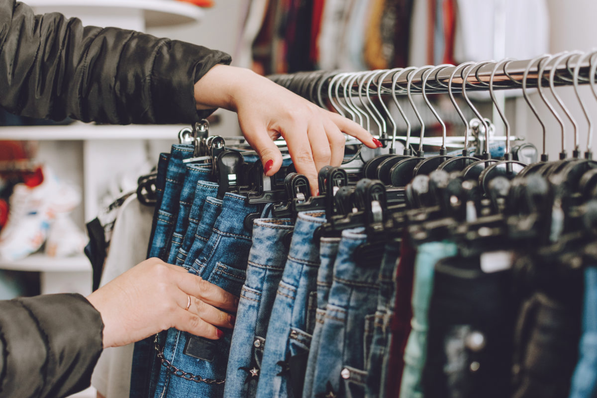Fast fashion concept. Woman chooses jeans in a store. Lots of clothes in the store. Fast Fashion Destroying Planet