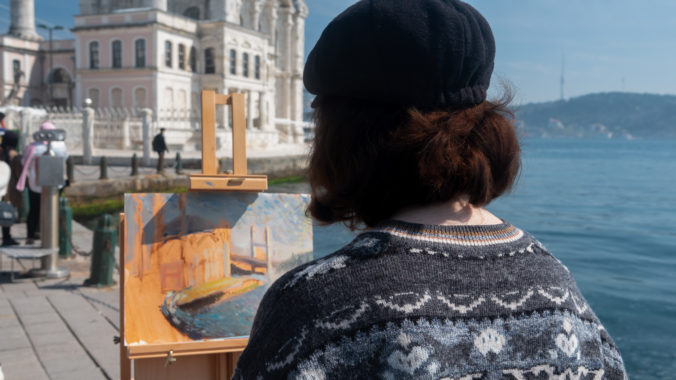 Young Caucasian female painter standing in front of the easel looks at the Ortaköy Mosque