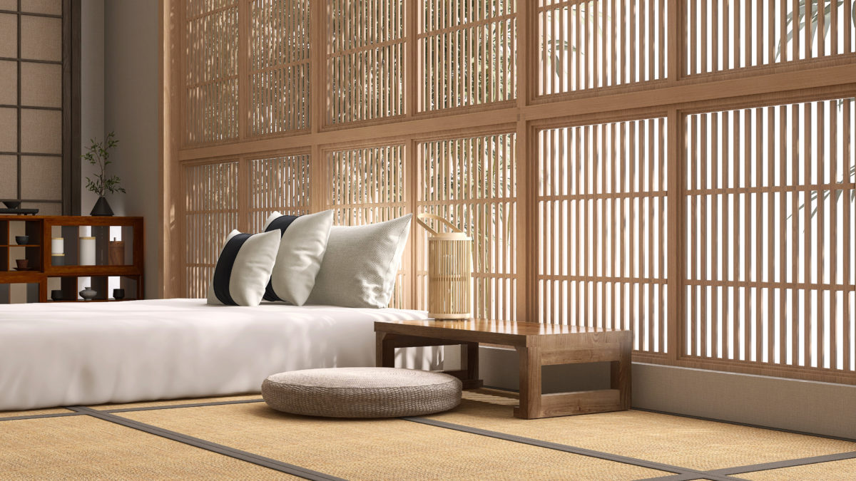 Wooden bedside table with lantern, pouf cushion seat by white bed sheet mattress, pillow on Japanese tatami mat in sunlight from shoji window blinds